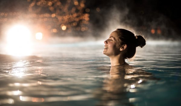 Young happy woman swimming in heated swimming pool during winter night.