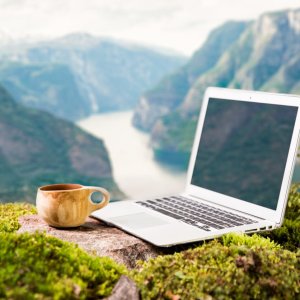 A freelancer's digital nomad's morning coffee with a Moka coffee maker, traditional wooden Finnish cup Kuksa and laptop on the Scandinavian landscape backdrop