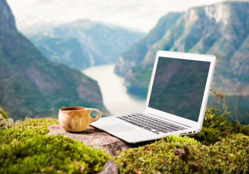 A freelancer's digital nomad's morning coffee with a Moka coffee maker, traditional wooden Finnish cup Kuksa and laptop on the Scandinavian landscape backdrop