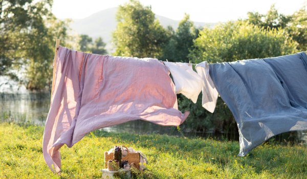 Pink and blue bedding sheet on forest background under the bright warm sun. Clean bed sheet hanging on clothesline at backyard.  Hygiene sleeping ware concept.