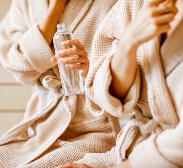 Women in bathrobes taking care of themselves, holding bottle in the SPA. Close-up view