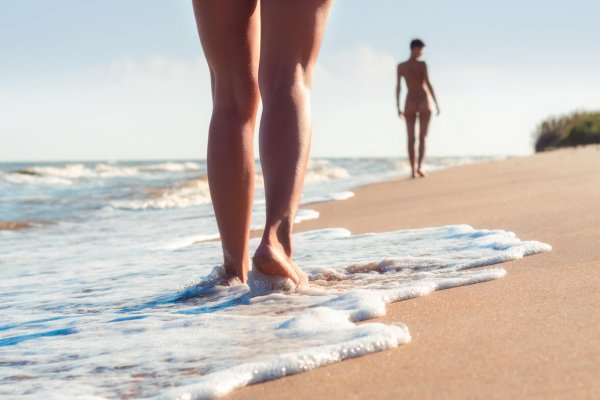 nude young girls walk on the beach in the waves of the surf on a summer day