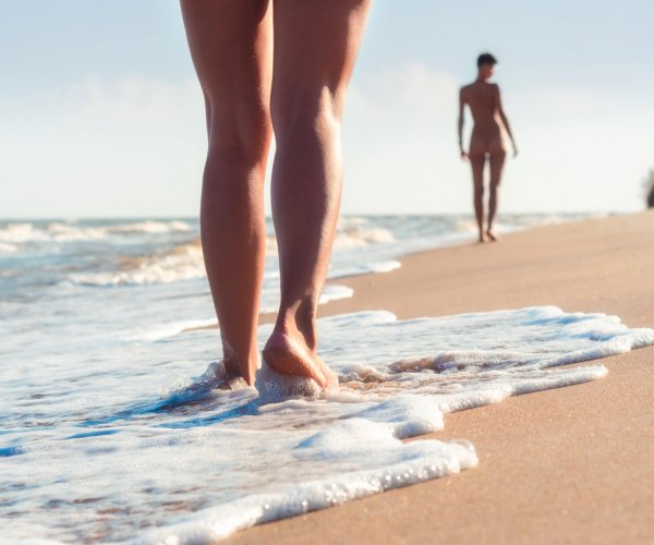 nude young girls walk on the beach in the waves of the surf on a summer day