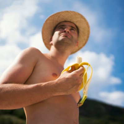 Young man with a straw hat eating banana.