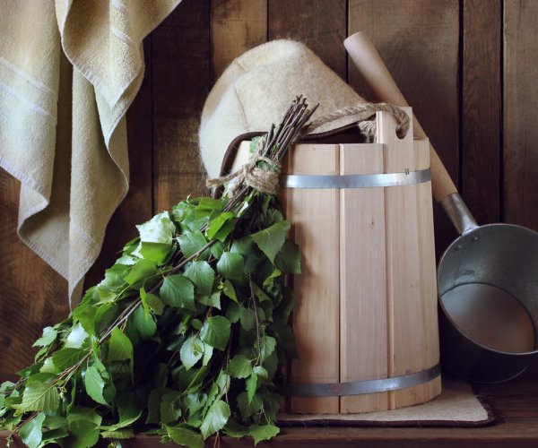 Bath broom made of birch and wooden bucket in a Russian bath close-up. Hat for bath and towel, bath accessories.