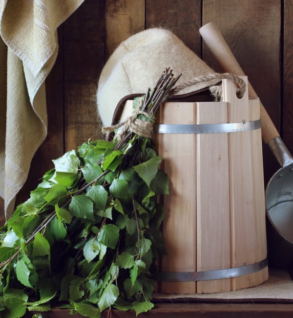 Bath broom made of birch and wooden bucket in a Russian bath close-up. Hat for bath and towel, bath accessories.